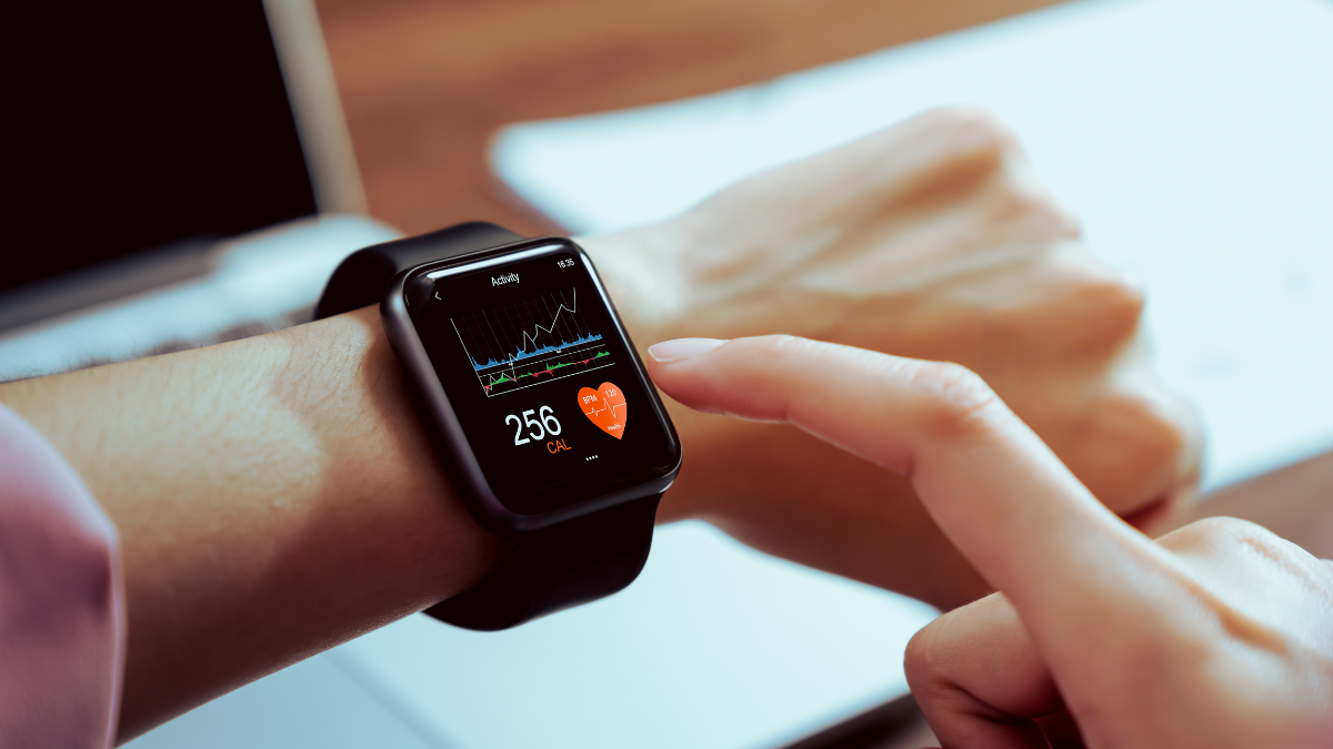 A person wearing a black smartwatch displaying heart rate and activity data, with another hand interacting with the screen.