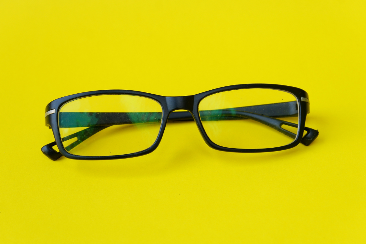 Black rectangular eyeglasses placed on a bright yellow surface.