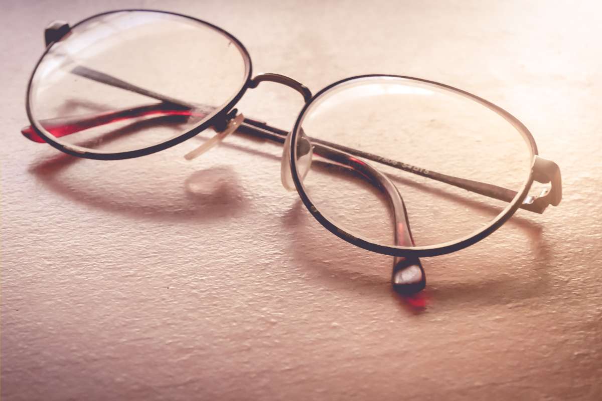 Close-up of round eyeglasses with thin frames placed on a surface, lit by soft natural light.