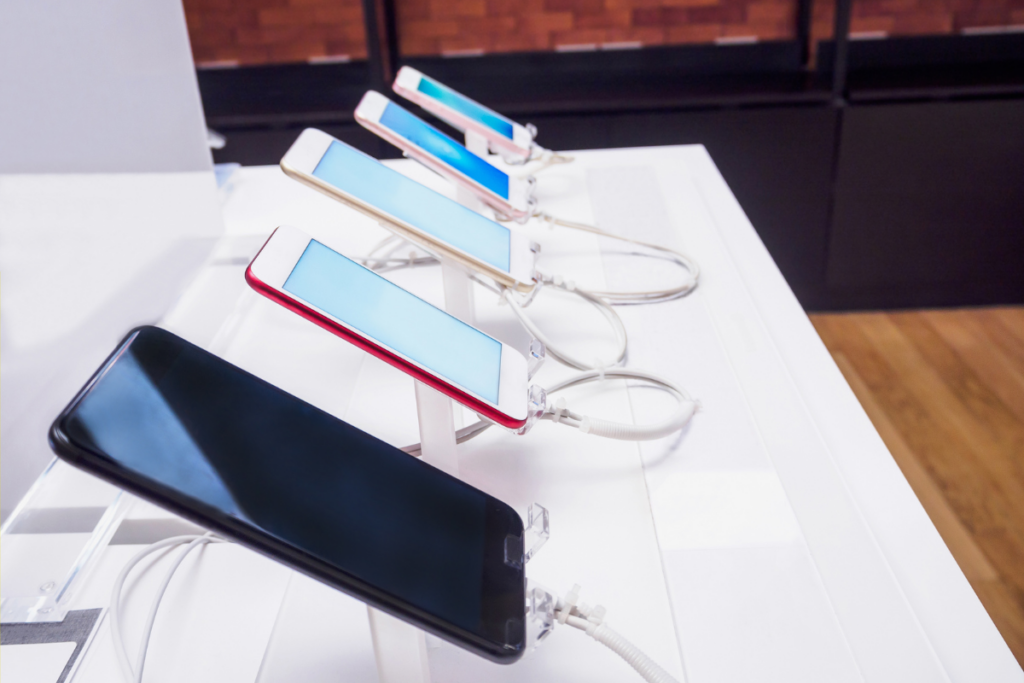 Row of smartphones in various colors displayed on a store counter, secured with anti-theft cables.