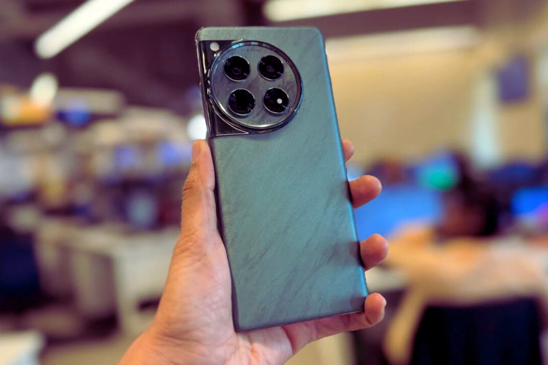 A hand holding a modern smartphone with a sleek design and a large circular camera module featuring multiple lenses on the back.