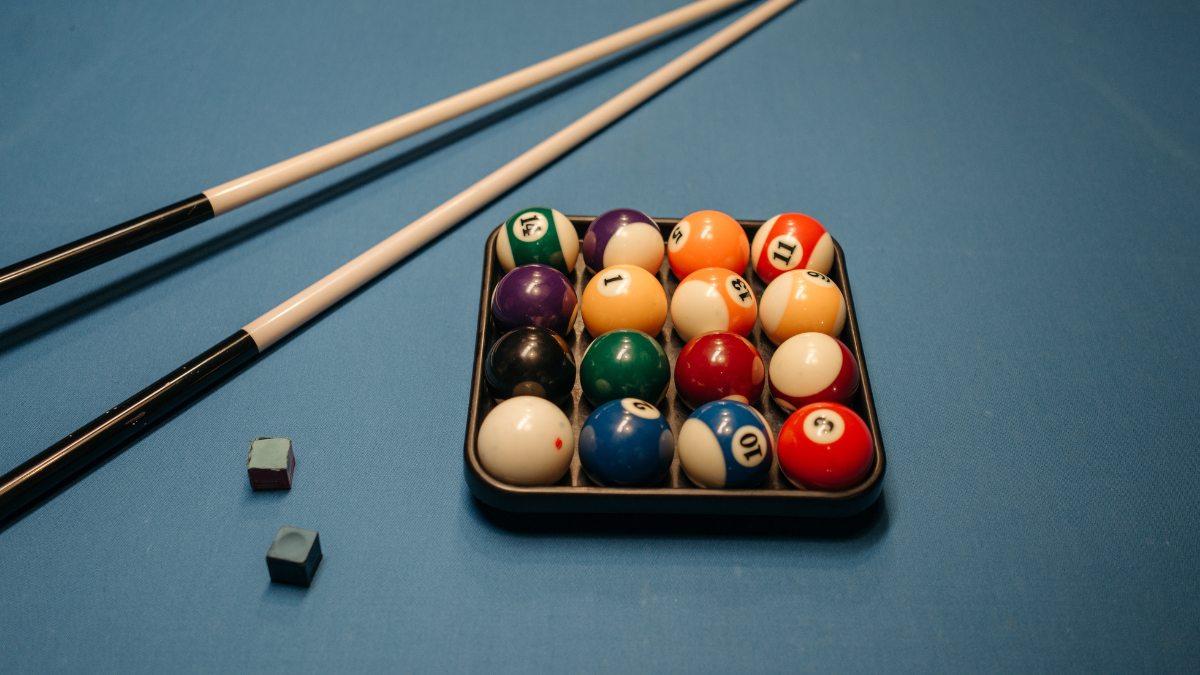 This image features a full set of pool balls neatly organized in a triangular rack on a blue billiard table, accompanied by two pool cues and two pieces of cue chalk.